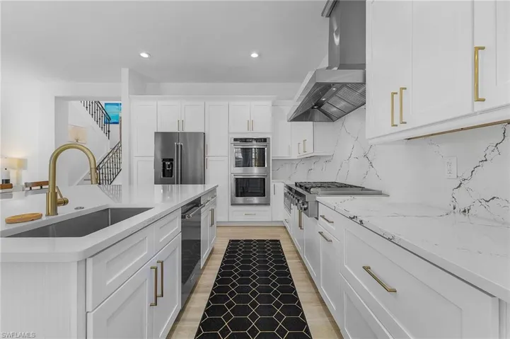 Kitchen with sink, exhaust hood, stainless steel appliances, tasteful backsplash, and white cabinets