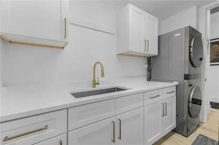 Washroom with cabinets, light hardwood / wood-style flooring, stacked washer / dryer, and sink