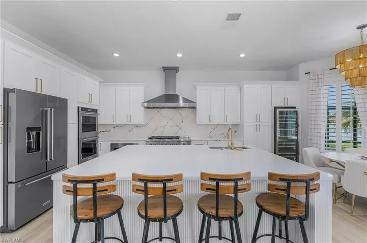 Kitchen with wine cooler, a center island with sink, exhaust hood, and appliances with stainless steel finishes