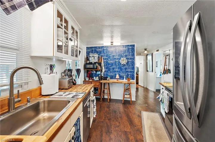 Kitchen with sink, dark wood-type flooring, wooden counters, appliances with stainless steel finishes, and white cabinets