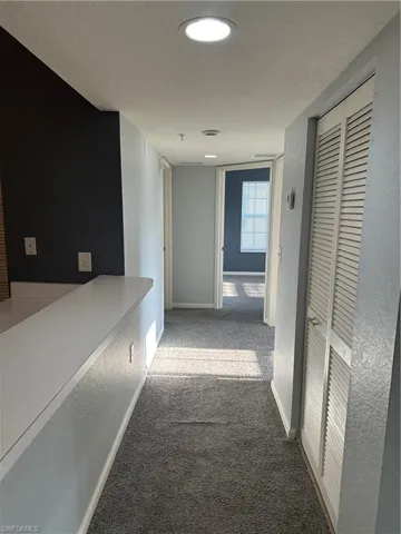 Recessed ceiling lighting illuminates a carpeted hallway with a louvered closet door