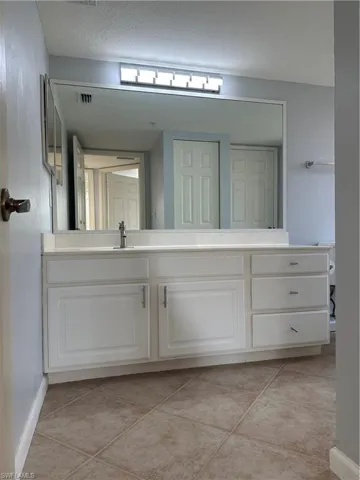 White vanity with shaker-style cabinetry, a built-in sink, and a large wall-mounted mirror