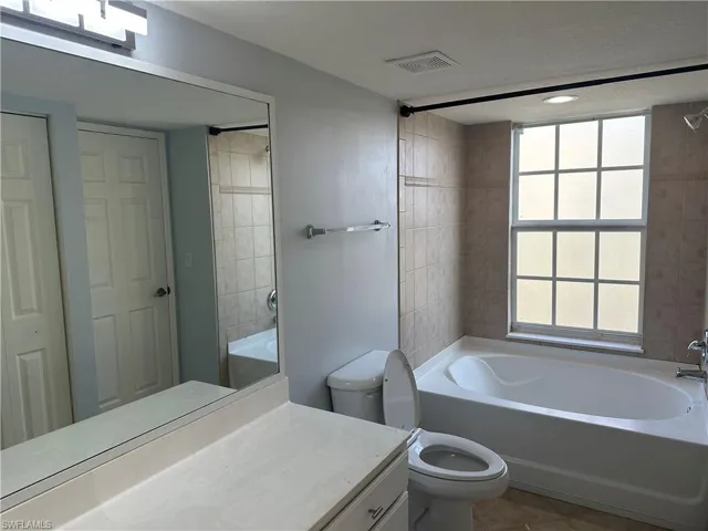 Built-in soaking tub with tiled surround, large vanity mirror, and window with privacy glazing