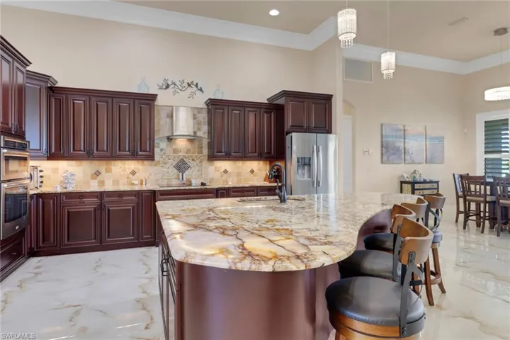Kitchen with appliances with stainless steel finishes, light marble finish floors, wall chimney exhaust hood, ornamental molding, and decorative light fixtures