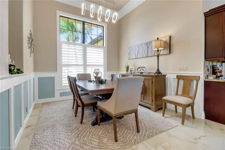 Dining area with a decorative wall, light marble finish floors, and wainscoting