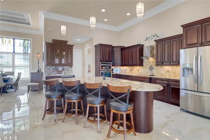 Kitchen with appliances with stainless steel finishes, wall chimney exhaust hood, light marble finish floors, crown molding, and decorative backsplash