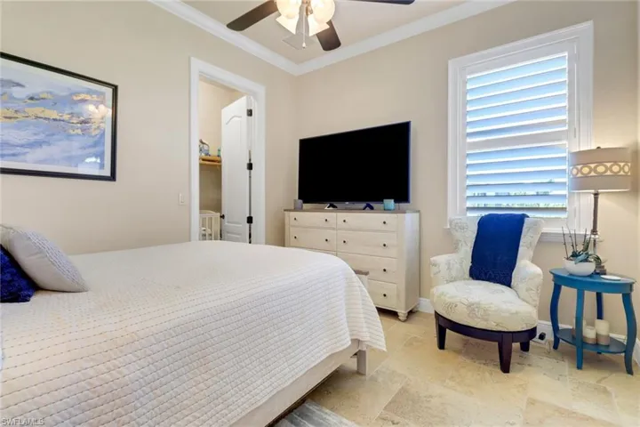Bedroom with stone tile flooring, ornamental molding, and a ceiling fan
