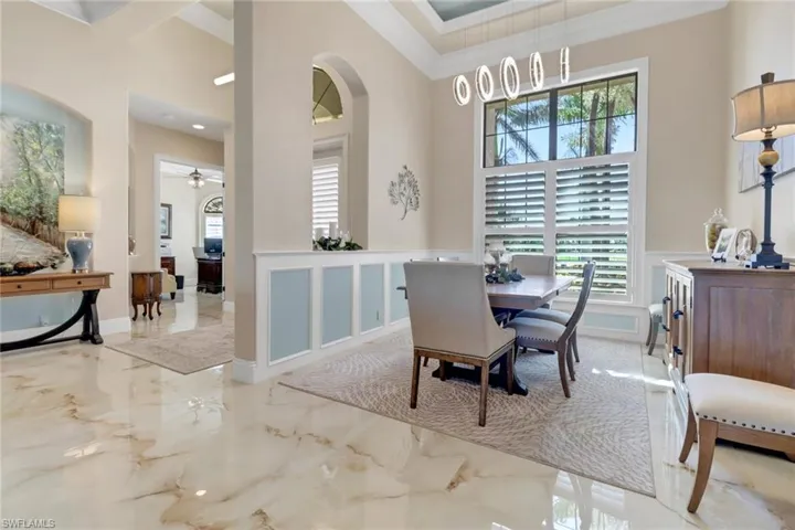 Dining area featuring a high ceiling, marble tiled flooring, healthy amount of natural light, wainscoting, and a decorative wall