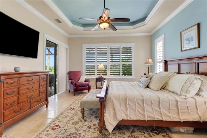 Bedroom with a raised ceiling, multiple windows, ornamental molding, and a ceiling fan