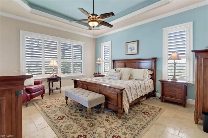 Bedroom with multiple windows, a raised ceiling, ornamental molding, and stone tile floors