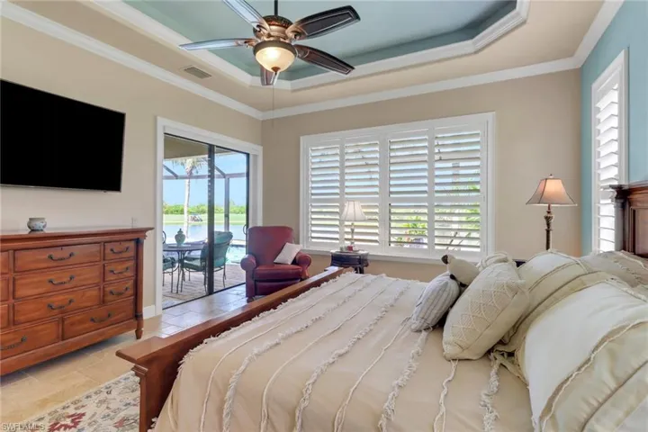Bedroom with a raised ceiling, access to exterior, ornamental molding, and ceiling fan