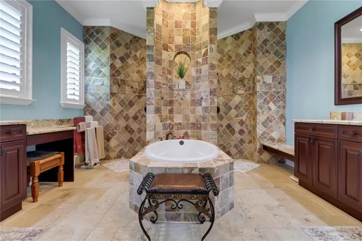 Full bathroom with stone tile flooring, crown molding, vanity, a bath, and tile walls