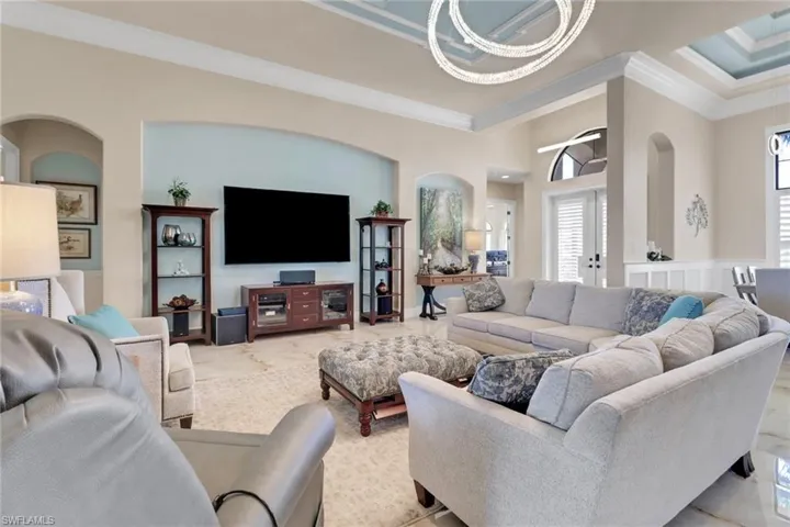 Living area with crown molding, a chandelier, light marble finish flooring, and arched walkways