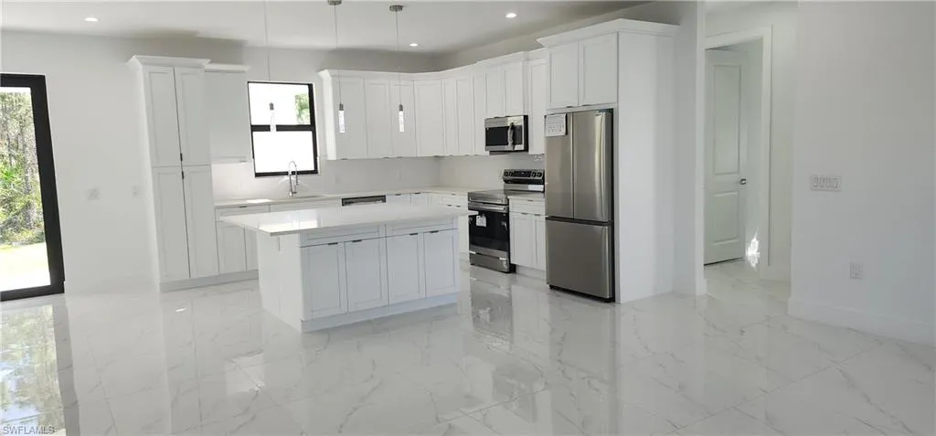 Kitchen with stainless steel appliances, island, white cabinets, and pendant lighting