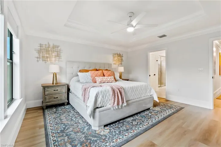Bedroom with ornamental molding, a raised ceiling, light wood-style floors, ceiling fan, and ensuite bathroom