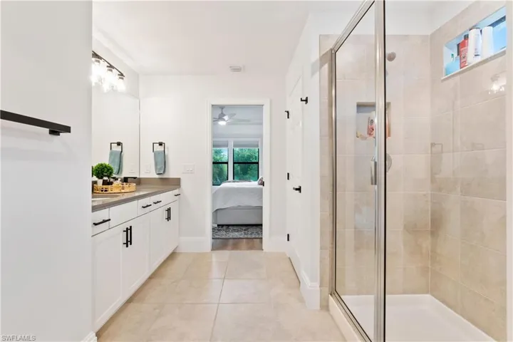 Ensuite bathroom with vanity, a shower stall, a ceiling fan, and tile patterned flooring