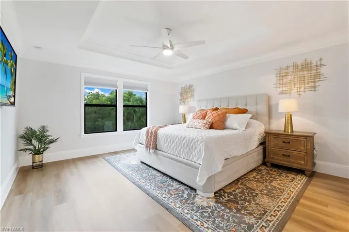 Bedroom featuring ornamental molding, wood finished floors, a raised ceiling, and ceiling fan