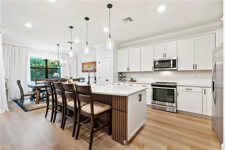 Kitchen featuring crown molding, appliances with stainless steel finishes, light wood finished floors, light countertops, and a kitchen bar
