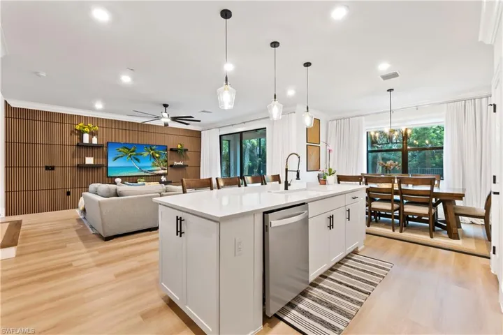 Kitchen featuring ornamental molding, light countertops, stainless steel dishwasher, light wood-type flooring, and an island with sink