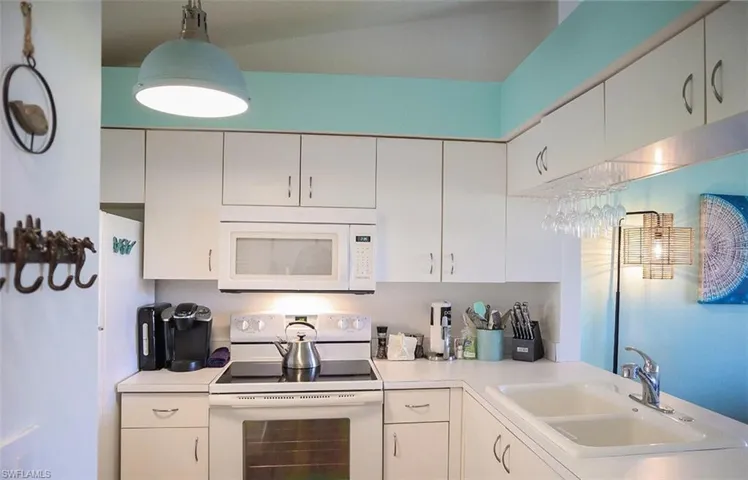 Kitchen with light countertops, a sink, white cabinetry, and white appliances