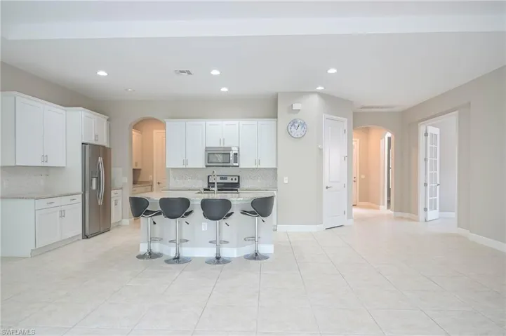 Kitchen with decorative backsplash, white cabinets, a kitchen island with sink, and stainless steel appliances
