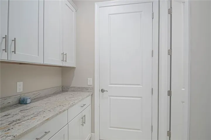 Bar featuring white cabinets and light stone counters