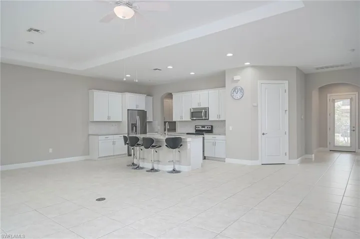Kitchen featuring tasteful backsplash, white cabinetry, appliances with stainless steel finishes, an island with sink, and a breakfast bar area