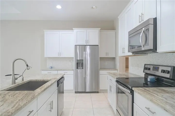 Kitchen featuring white cabinets, stainless steel appliances, sink, and light stone countertops