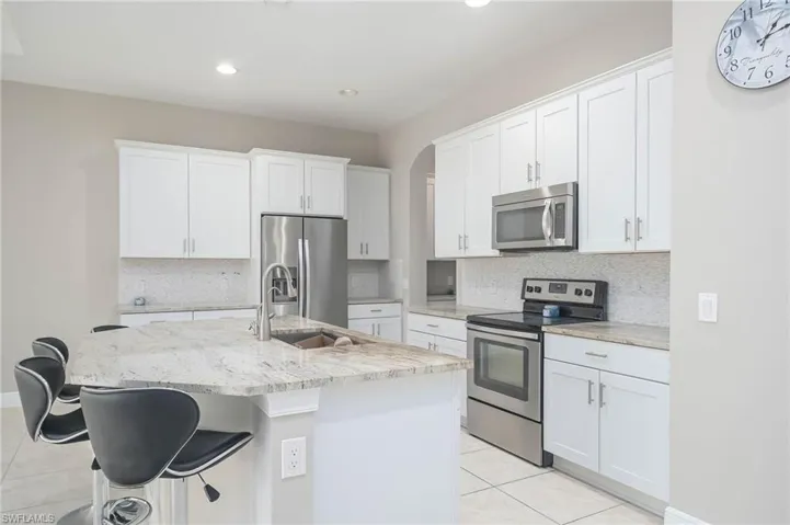 Kitchen with white cabinetry, appliances with stainless steel finishes, sink, and a kitchen island with sink