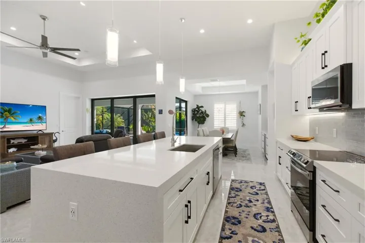 Kitchen with appliances with stainless steel finishes, white cabinets, a tray ceiling, hanging light fixtures, and light stone counters