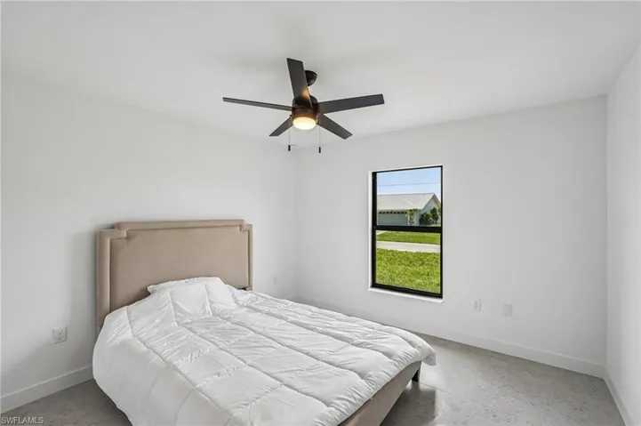 Clean white walls define this room featuring a window with black trim, a ceiling fan with integrated lighting, and polished concrete flooring
