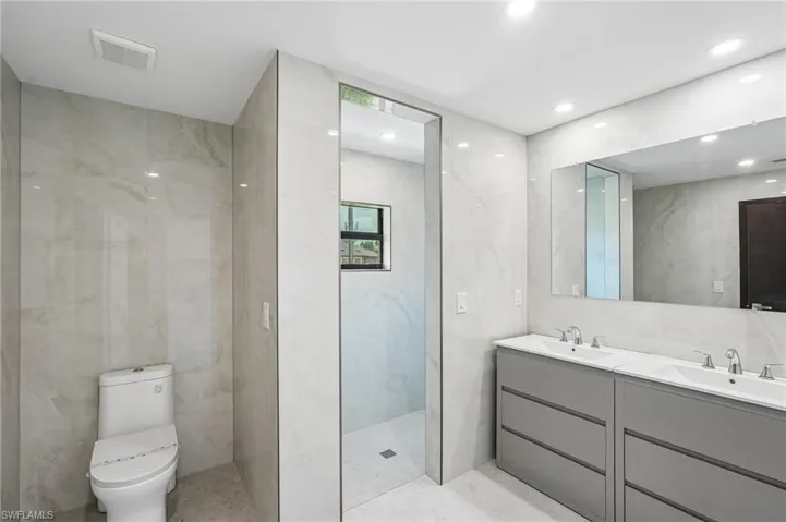 Contemporary bathroom featuring a dual vanity with undermount sinks and chrome fixtures, a spacious walk-in shower, a toilet, recessed lighting, and large format tiled walls