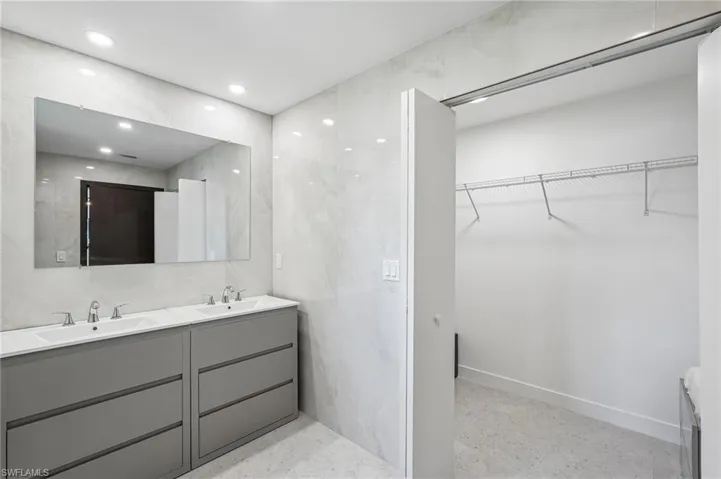 Bathroom featuring a dual vanity with gray cabinetry and integrated sinks, a large wall-mounted mirror, and recessed lighting