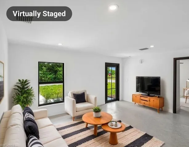 Bright living space featuring light gray flooring, white walls, black trim windows, a black frame exterior door with glass panels, and recessed ceiling lighting