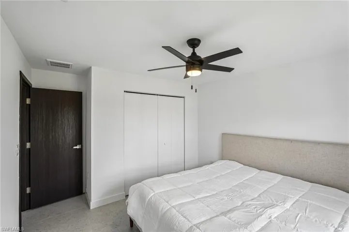 Bedroom featuring a dark wood-finish entry door, a ceiling fan with integrated lighting, and a neutral upholstered headboard