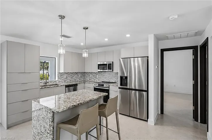 Modern kitchen featuring light cabinetry, stainless steel appliances, a center island with stone countertop, a tile backsplash, and pendant lighting