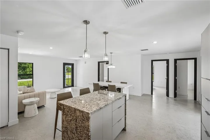 Open-concept living space featuring a kitchen island with stone countertop, recessed lighting, pendant lights, and light-toned flooring