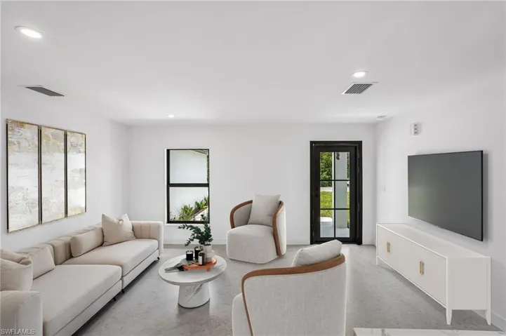 Spacious living area featuring light-colored flooring, recessed lighting, and a dark-framed glass paneled door