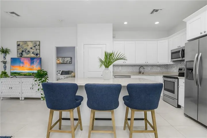Updated kitchen with stainless steel appliances, tasteful backsplash, breakfast bar, and white cabinetry