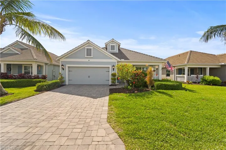 View of front of property with a front yard, an attached garage, a tile roof, and decorative driveway