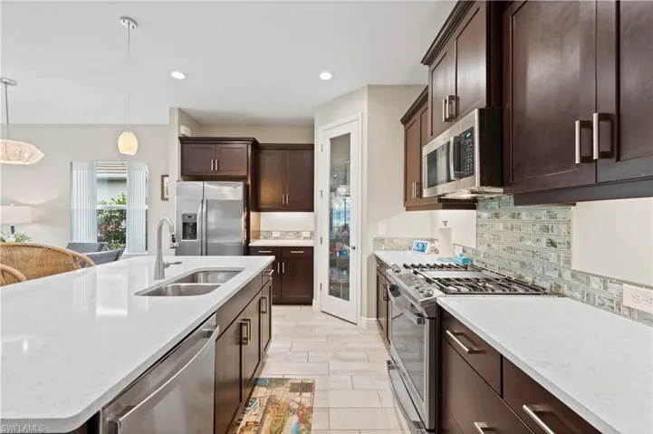 Kitchen with dark brown cabinetry, backsplash, stainless steel appliances, pendant lighting, and a sink