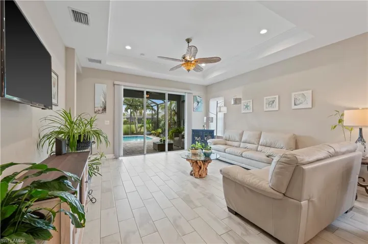 Living room featuring ornamental molding, visible vents, ceiling fan, and a raised ceiling