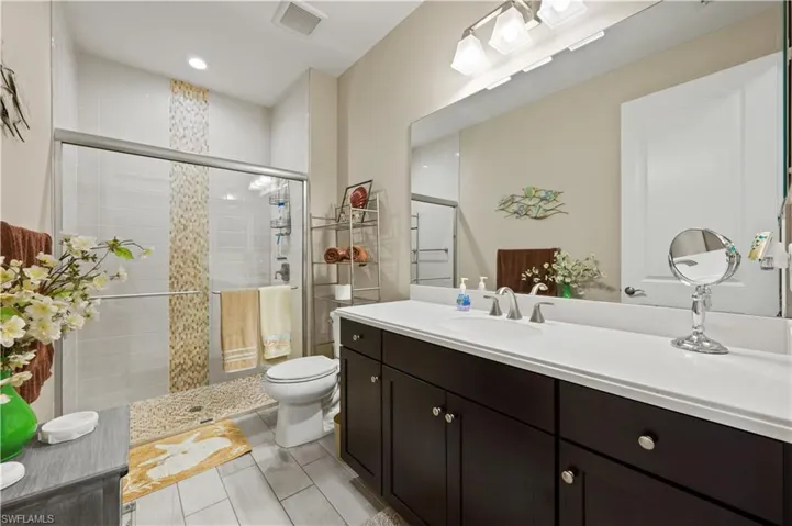 Full bath with vanity, visible vents, a tile shower, and toilet