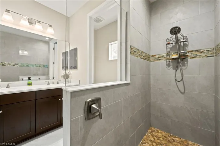 Full bath featuring double vanity, visible vents, a sink, and a tile shower