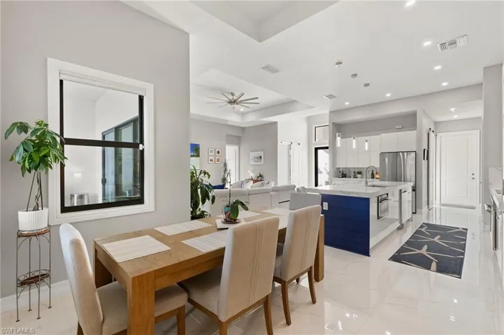 Dining area featuring a raised ceiling, light marble finish floors, recessed lighting, ceiling fan, and plenty of natural light