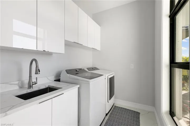 Laundry room with light marble finish flooring, cabinet space, and washing machine and clothes dryer