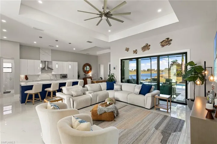 Living room featuring a tray ceiling, a water view, a ceiling fan, a towering ceiling, and recessed lighting