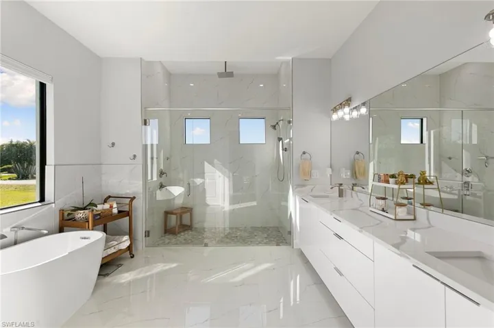 Bathroom featuring double vanity, a marble finish shower, a freestanding tub, and healthy amount of natural light