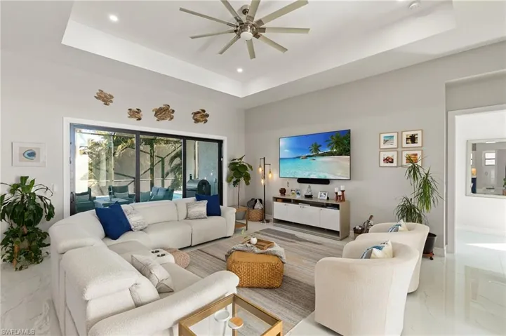 Living area featuring a raised ceiling, light marble finish floors, recessed lighting, and a high ceiling