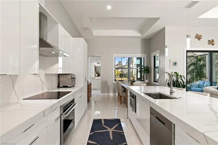 Kitchen with modern cabinets, hanging light fixtures, light stone countertops, a tray ceiling, and recessed lighting